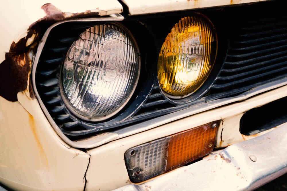 Nahaufnahme eines Oldtimers mit verrostetem Kühlergrill, einem klaren und einem gelb getönten Scheinwerfer, passend für ein Gutachten