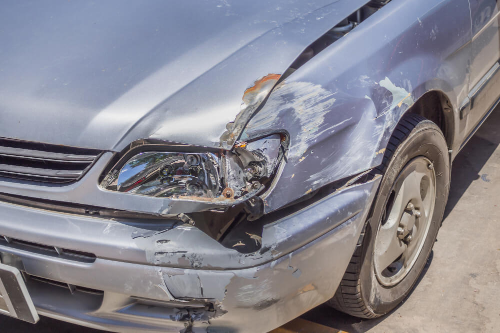 Ein silbernes Auto mit beschädigtem vorderen Kotflügel, Scheinwerfer und Stoßstange nach einem Unfall