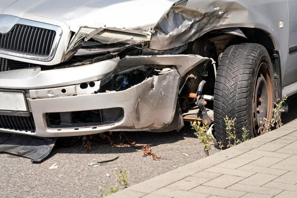 Ein silbernes Auto mit plattem Reifen und zerbeulter Front steht als automatisch gespeicherter Entwurf am Bordstein zwischen Unkraut