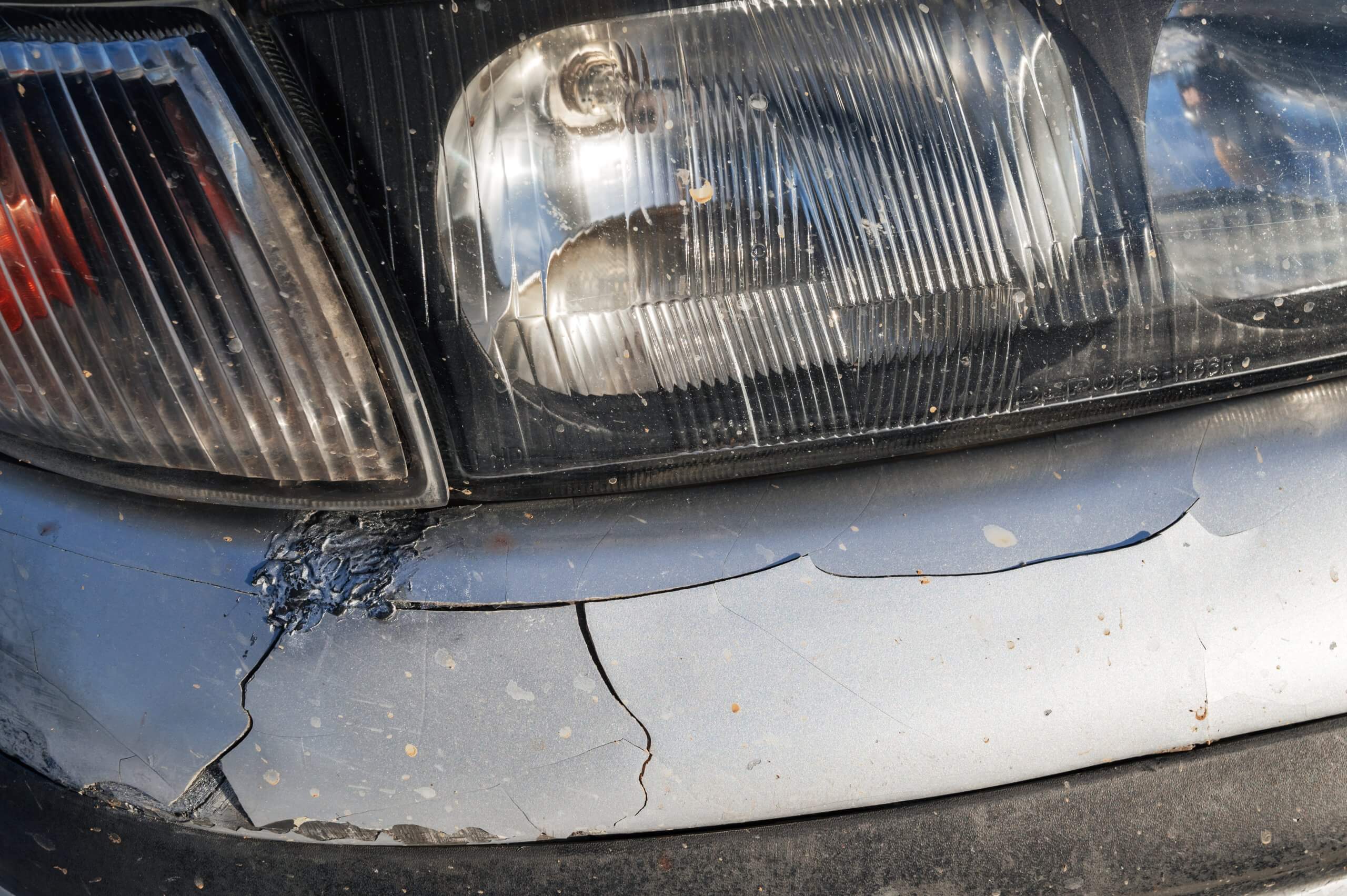 Rissiger Stoßfänger unter einem zerkratzten Scheinwerfer an einem silbernen Auto, sichtbar als automatisch gespeicherter Entwurf
