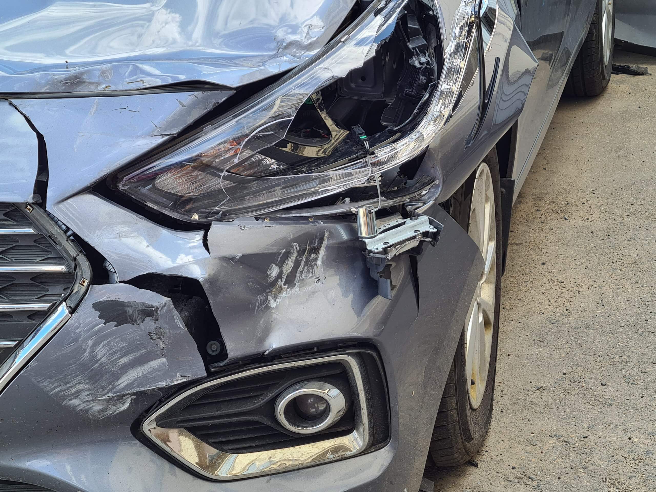 Ein silbernes Auto mit starken Schäden vorne links, eingedrücktem Kotflügel und zerbrochenem Scheinwerfer