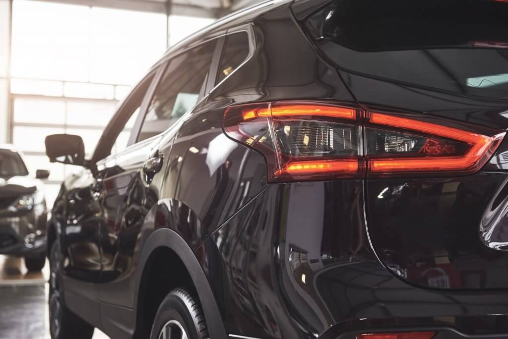 Das Heck eines schwarzen SUVs mit leuchtenden Rücklichtern steht als automatisch gespeicherter Entwurf in einem hellen Autohaus
