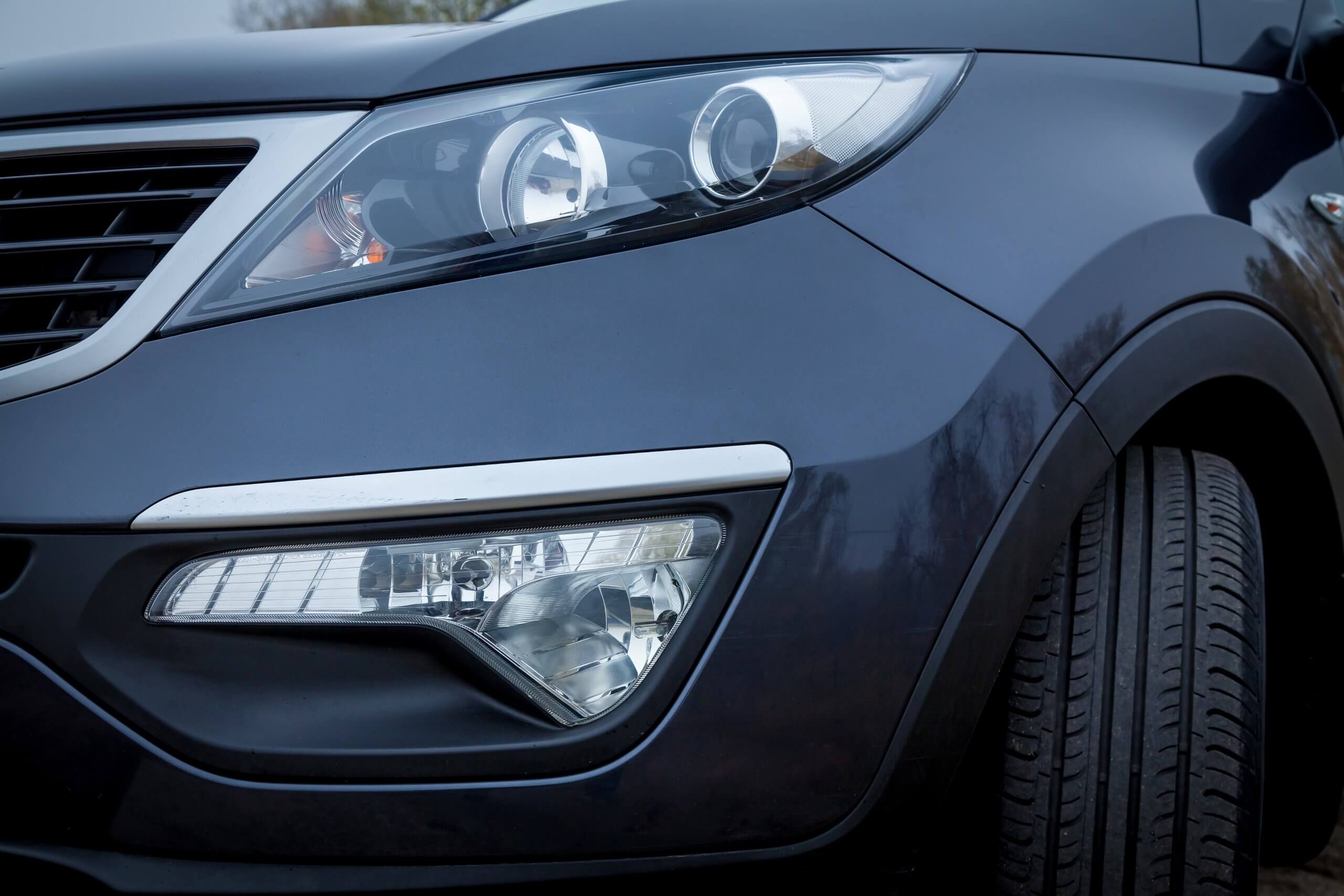 Nahaufnahme des vorderen linken Scheinwerfers und Reifens eines dunklen Autos mit Details der Automatisch gespeicherten Entwurfskarosserie