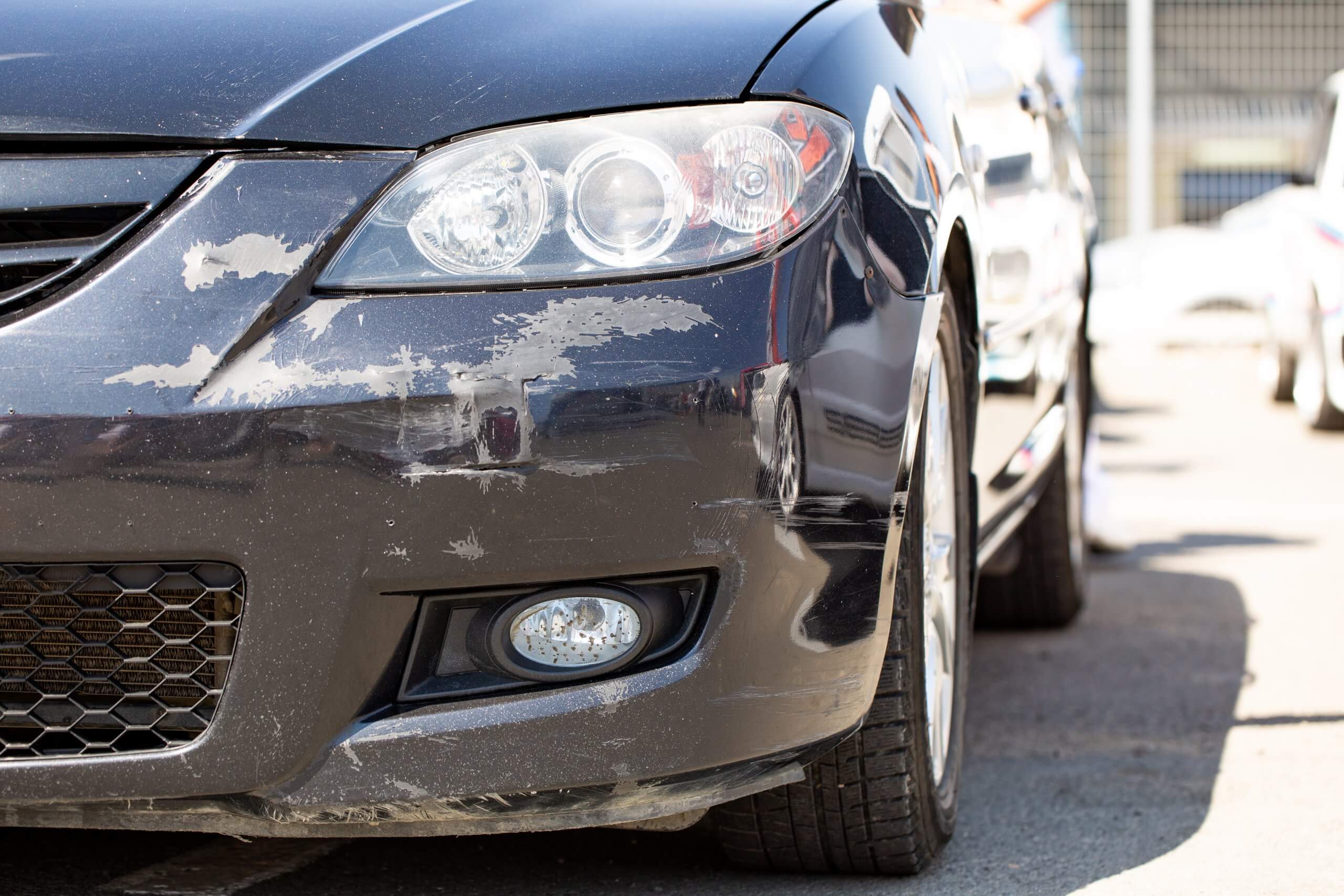 Nahaufnahme der zerkratzten vorderen Stoßstange eines schwarzen Autos, ein automatisch gespeicherter Entwurf steht draußen in der Sonne