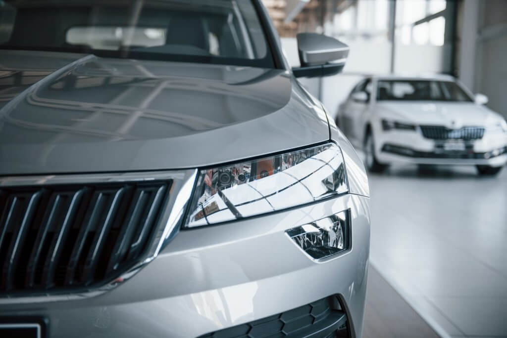 Nahaufnahme von Frontscheinwerfer und Kühlergrill eines silbernen Autos im Showroom, mit dem Label Automatisch gespeicherter Entwurf