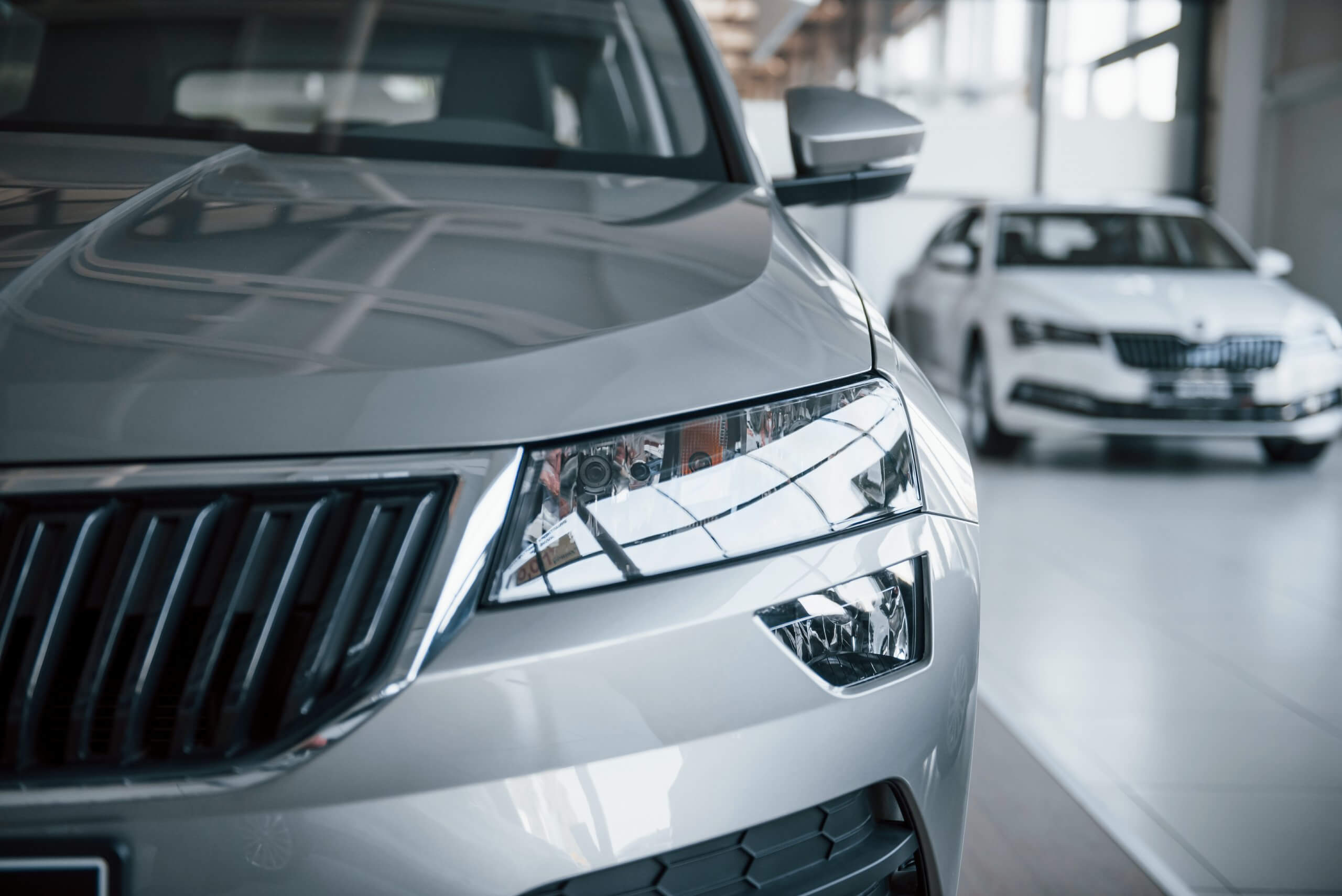 Nahaufnahme von Frontscheinwerfer und Kühlergrill eines silbernen Autos im Showroom, mit dem Label Automatisch gespeicherter Entwurf