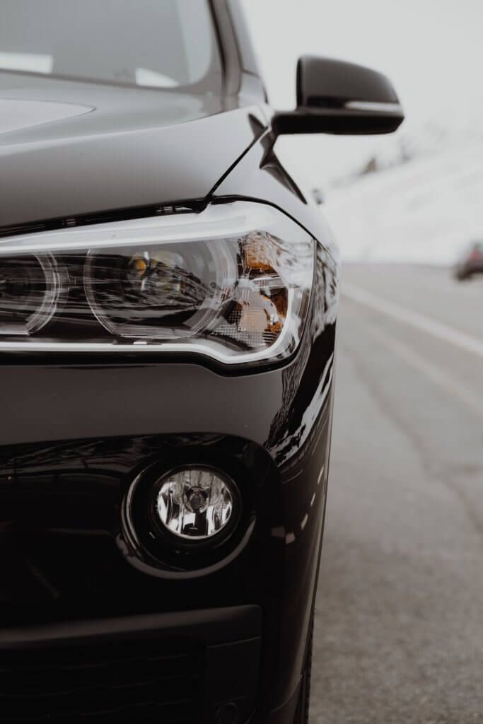 Detailansicht des linken Frontscheinwerfers und Kühlergrills eines schwarzen Autos als automatisch gespeicherter Entwurf vor unscharfem Straßenhintergrund