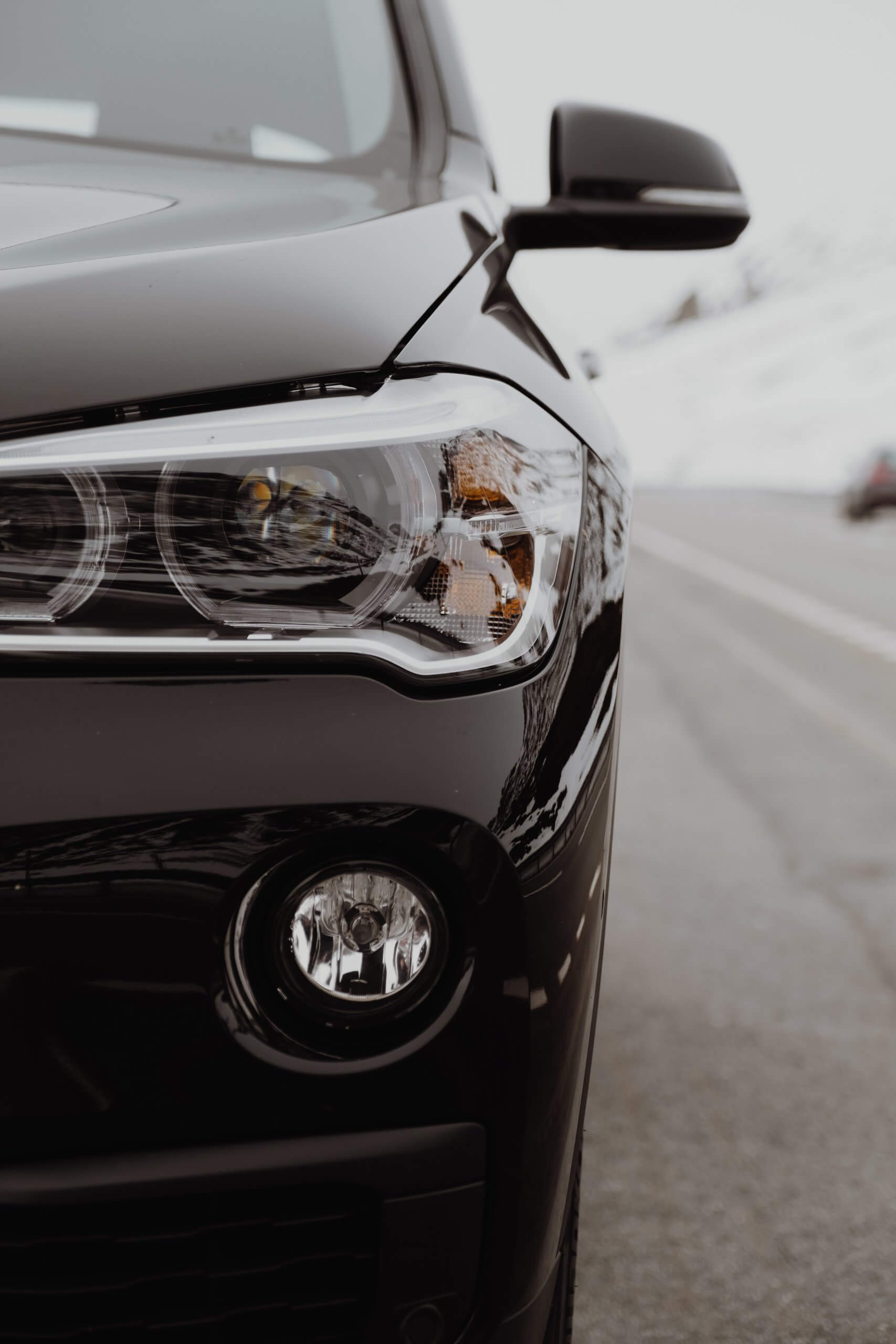 Detailansicht des linken Frontscheinwerfers und Kühlergrills eines schwarzen Autos als automatisch gespeicherter Entwurf vor unscharfem Straßenhintergrund